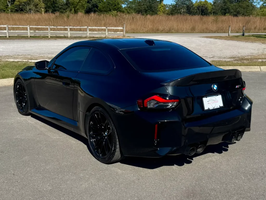 2025 BMW M2 black exterior rear three-quarter view with quad exhaust and sporty lines.