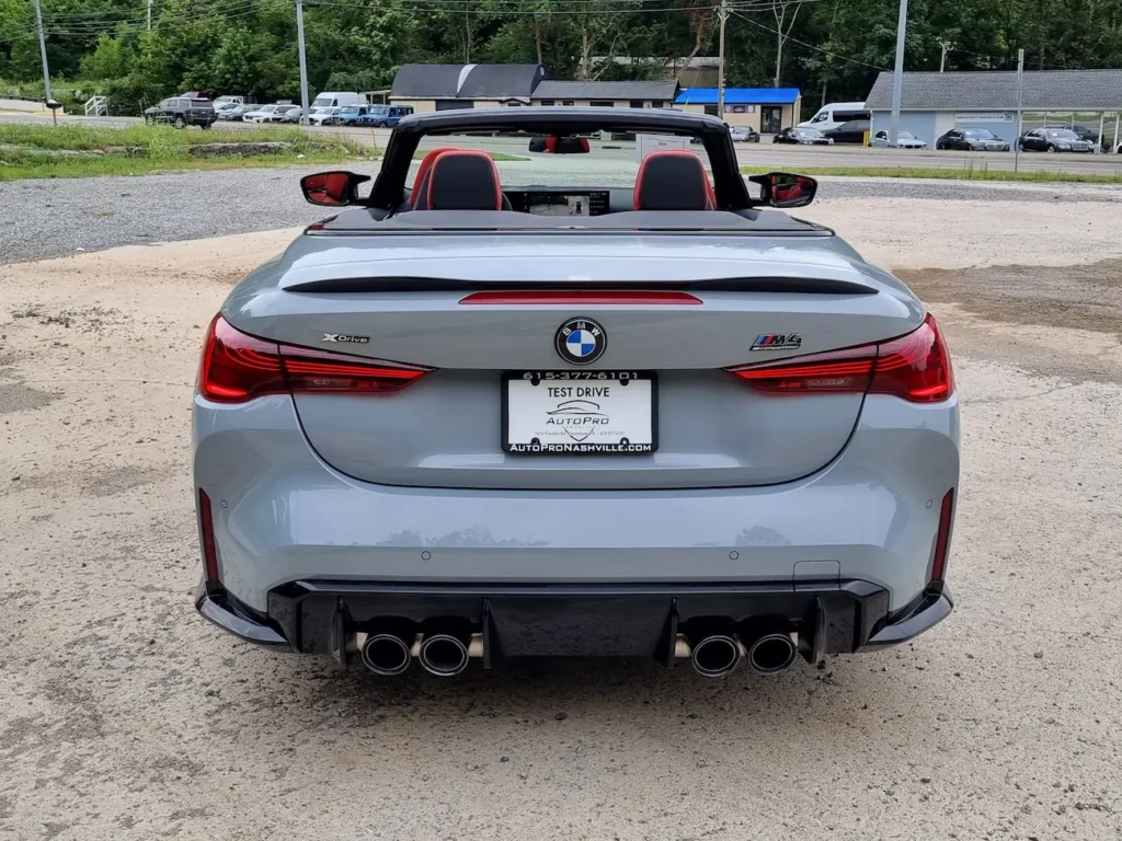 Rear view of 2025 BMW M4 Competition Convertible in Skyscraper Grey with quad exhaust and red interior.