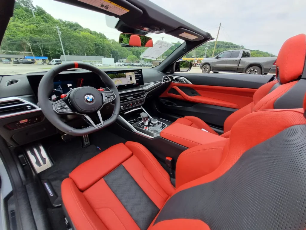 Interior of 2025 BMW M4 Competition Convertible with red and black M Sport seats and digital cockpit.