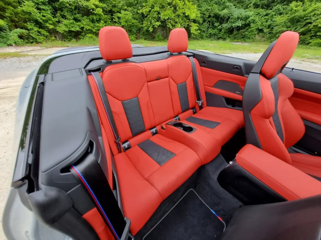 Rear seat area of 2025 BMW M4 Competition Convertible with red leather upholstery and M seatbelts.