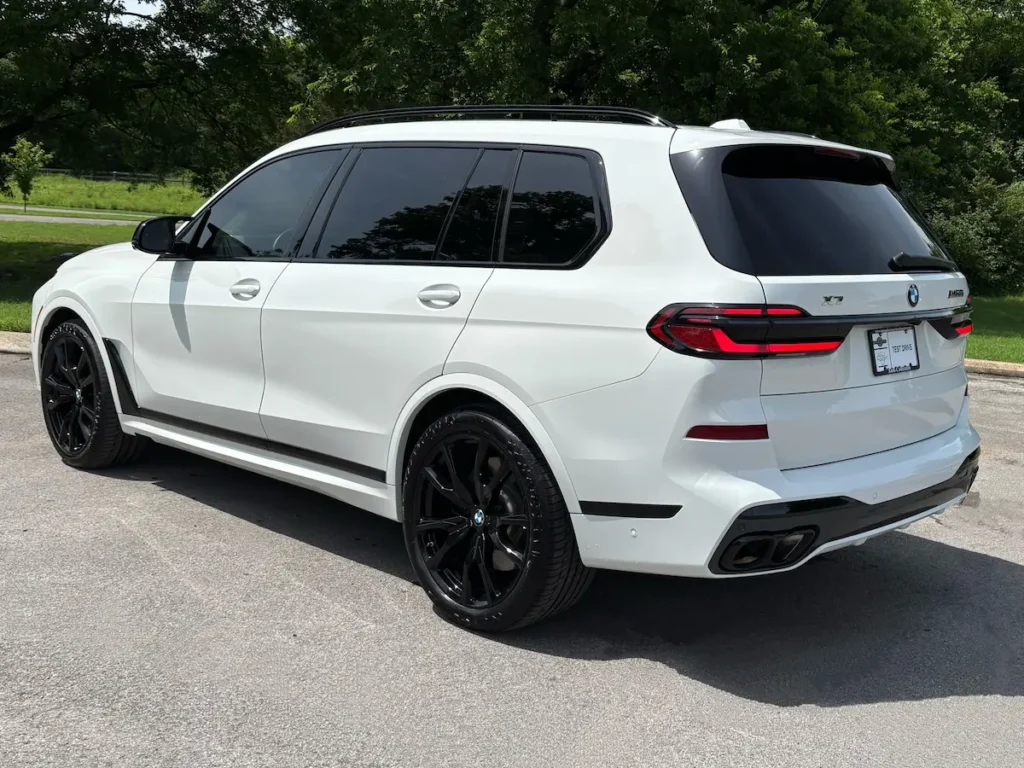 Rear three-quarter view of a white 2025 BMW X7 M60i three-row luxury SUV
