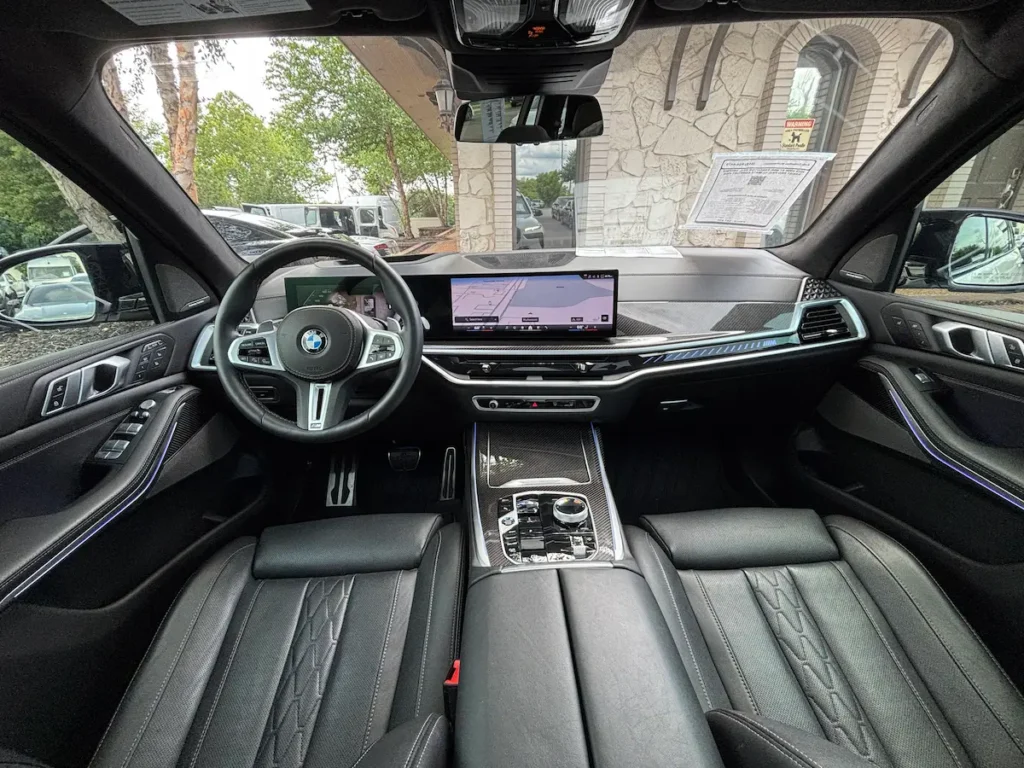 2025 BMW X7 M60i front interior with curved display, leather seats, and ambient lighting