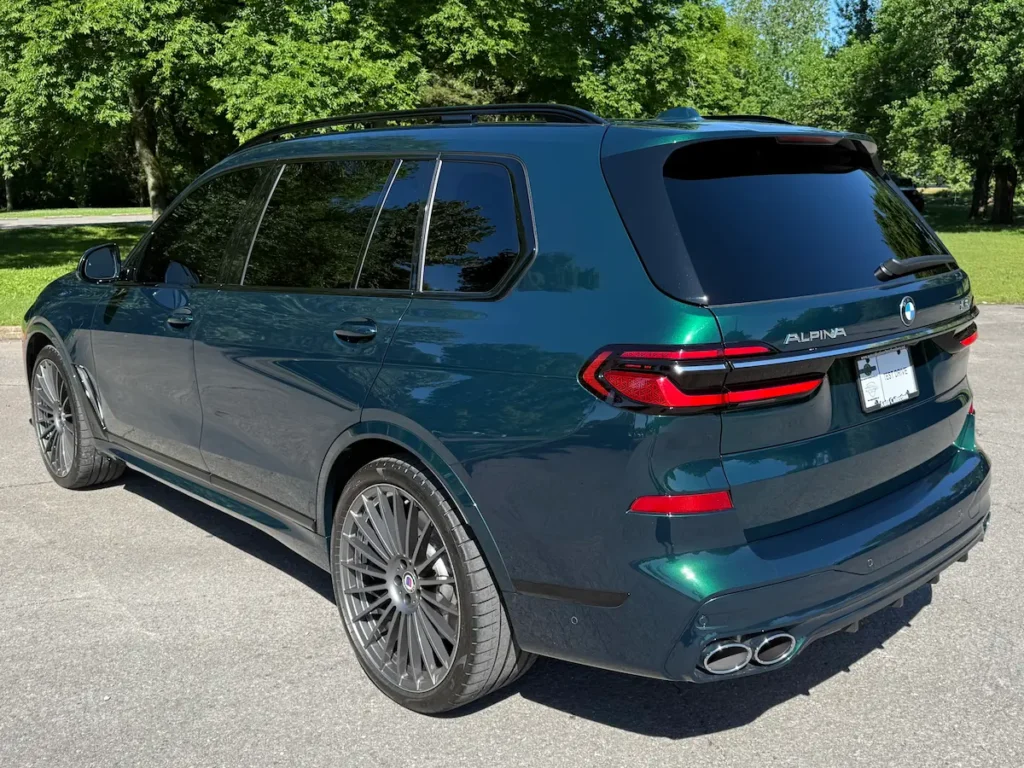 2025 BMW XB7 Alpina green exterior rear three-quarter view with quad exhaust and LED lighting.