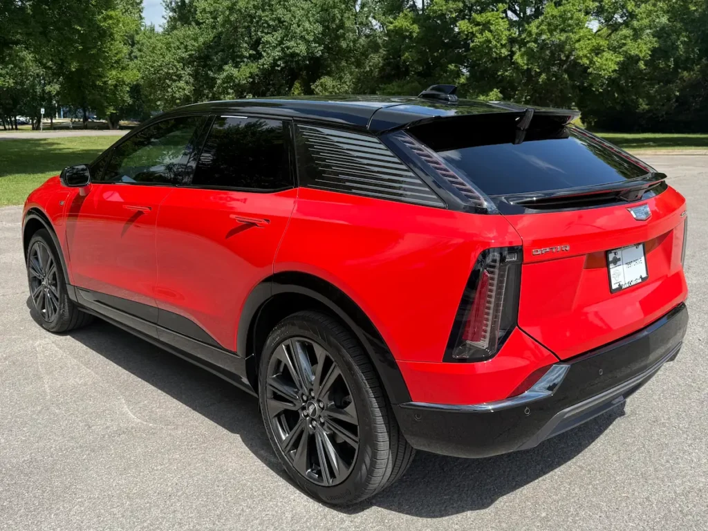 Rear exterior angle of a 2025 Cadillac Optiq in red showing the sculpted taillights, black roof, and sleek EV styling.