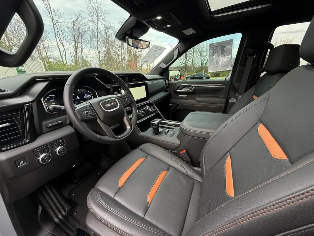 Interior cabin of a 2025 GMC Sierra 1500 AT4 with leather seats and digital displays.