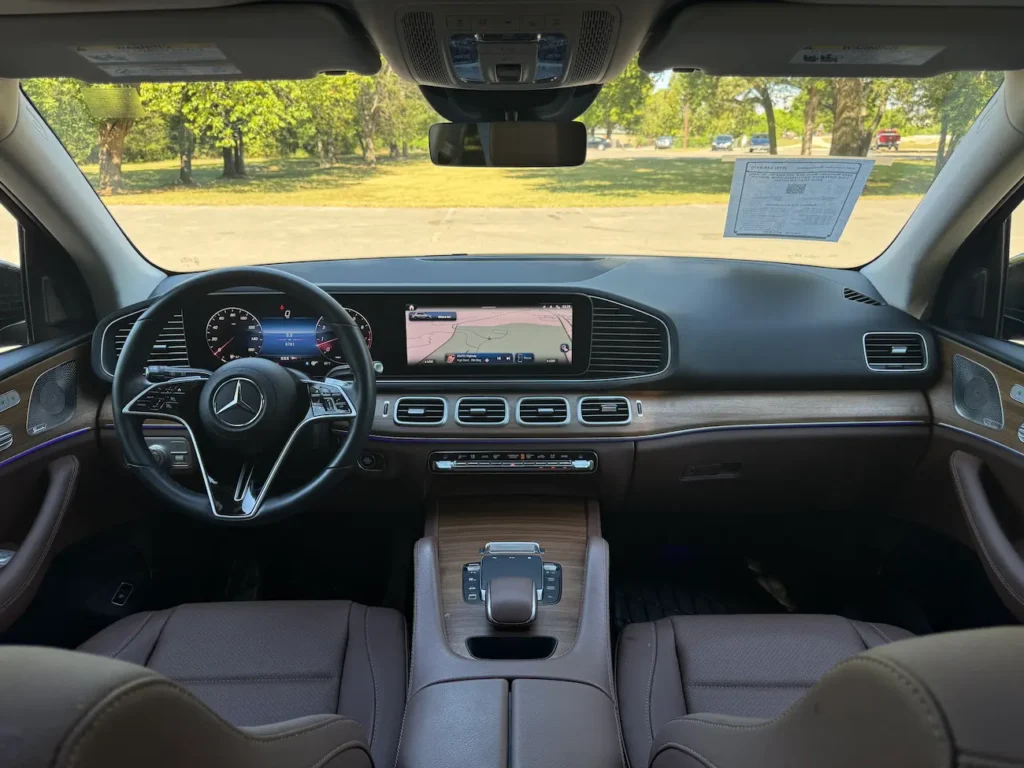 Interior front cabin of 2025 Mercedes-Benz GLE 350 showing steering wheel, dual MBUX screens, and wood trim.