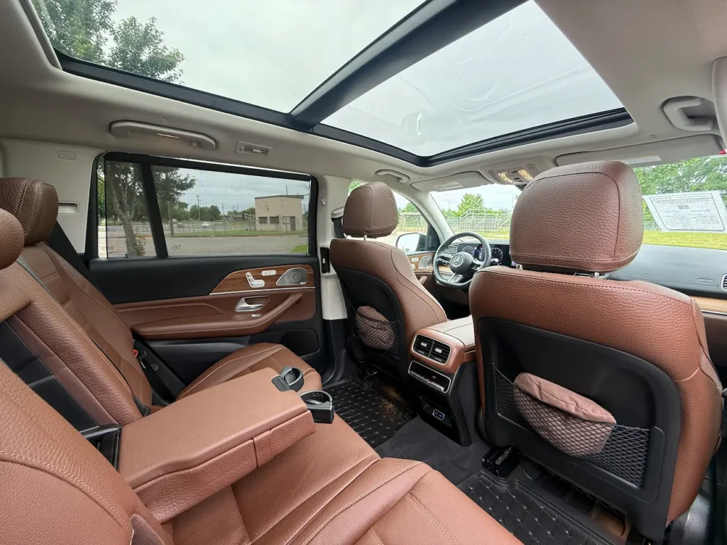 Rear interior of 2025 Mercedes-Benz GLS 450 with brown leather seats, panoramic sunroof, and ambient lighting.