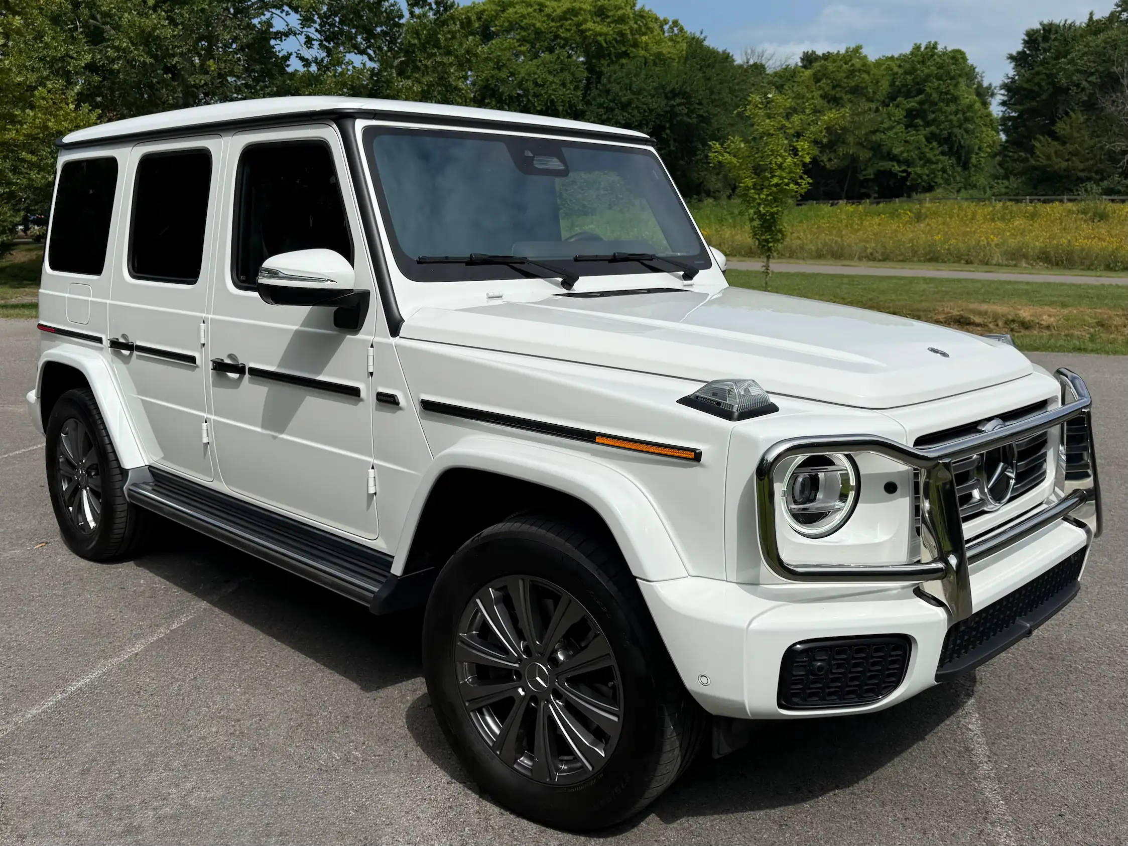 White 2025 Mercedes-Benz G 550 in front three-quarter view with round headlights, a front brush guard and side steps.