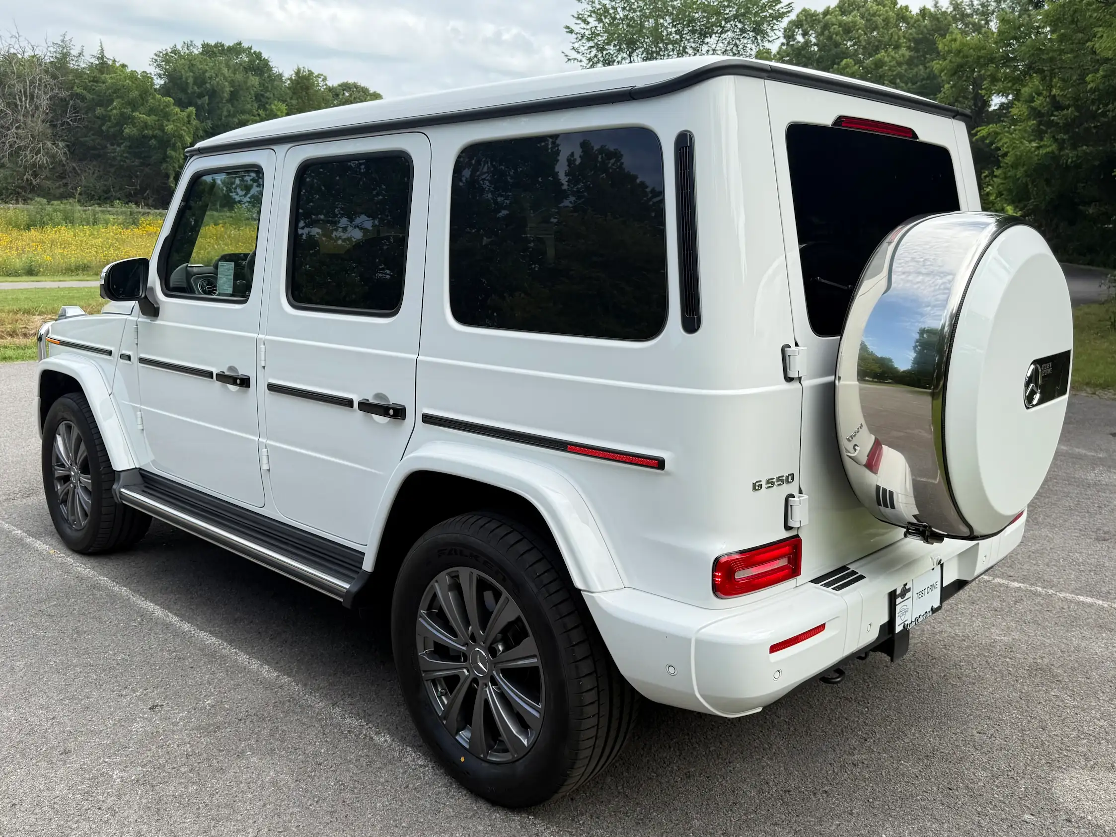White 2025 Mercedes-Benz G 550 viewed from the rear corner, showing its spare-wheel cover, G 550 badge and side steps.
