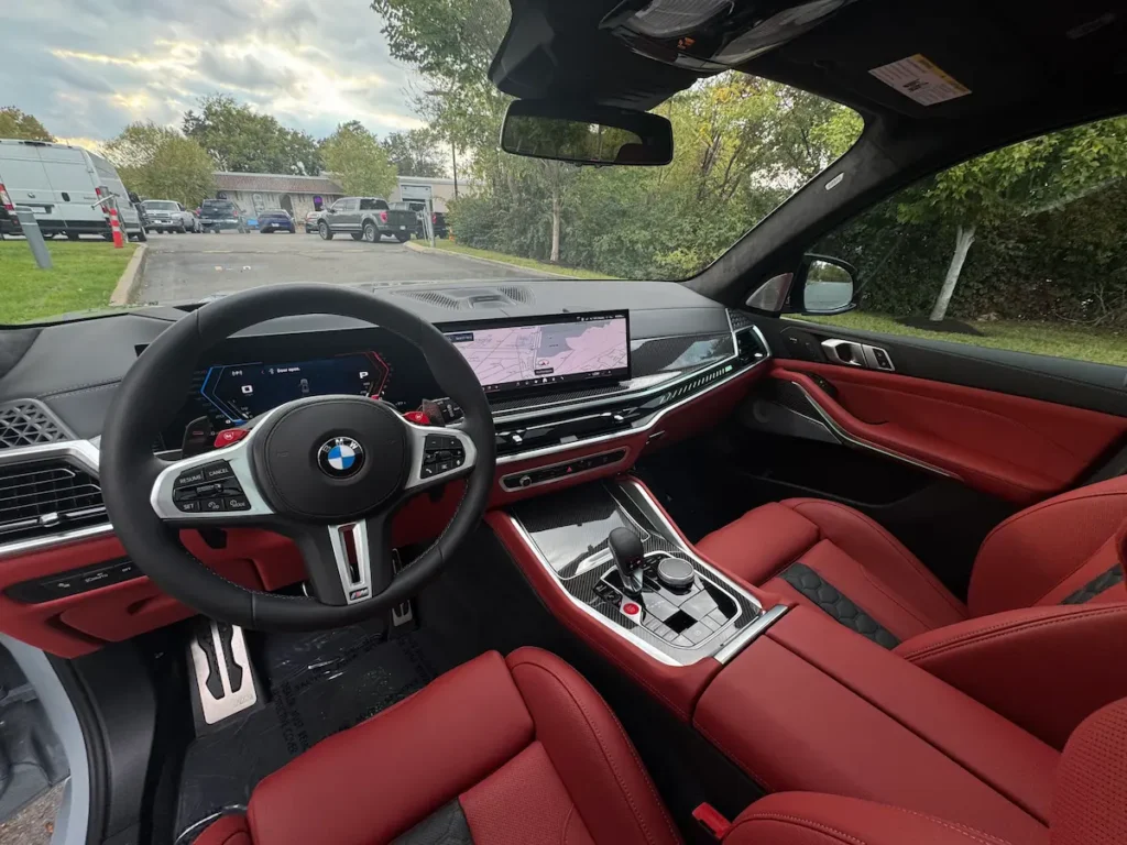 2026 BMW X5 M cabin with red leather seats, digital gauges, carbon-fiber trim, and large display.