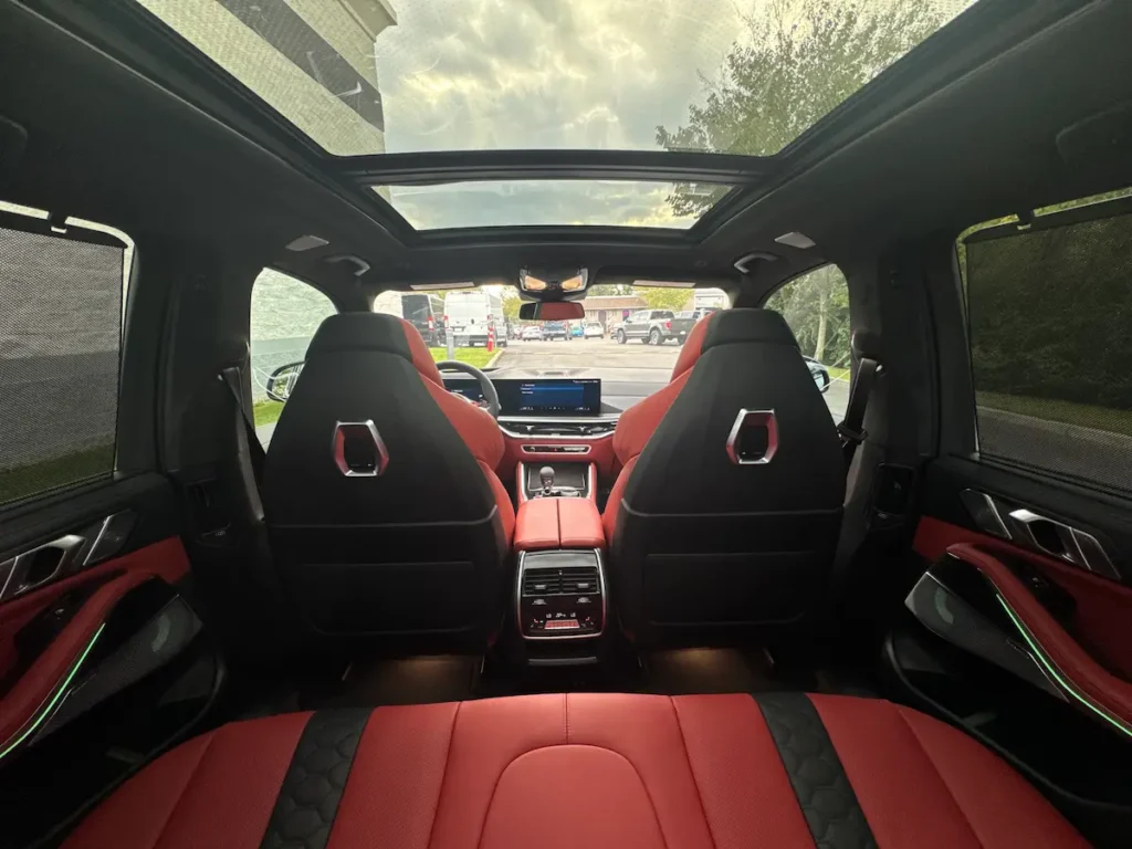2026 BMW X5 M rear interior with red leather seats, ambient lighting, and panoramic glass roof.