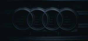 A close-up photo of a black and silver Audi logo on the front grille of a car.