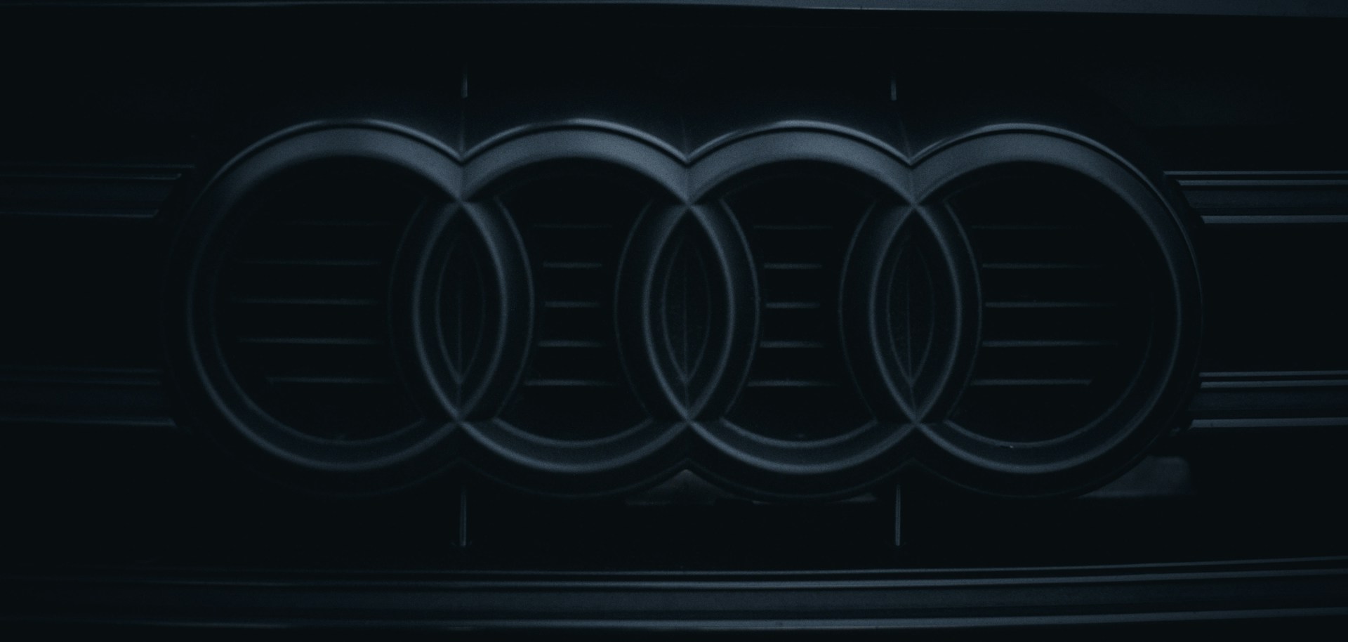 A close-up photo of a black and silver Audi logo on the front grille of a car.