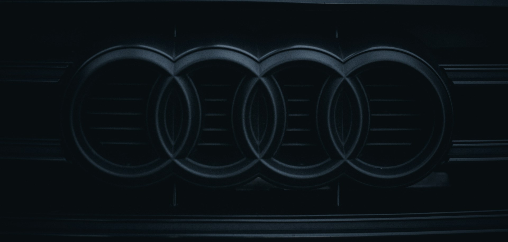 A close-up photo of a black and silver Audi logo on the front grille of a car.