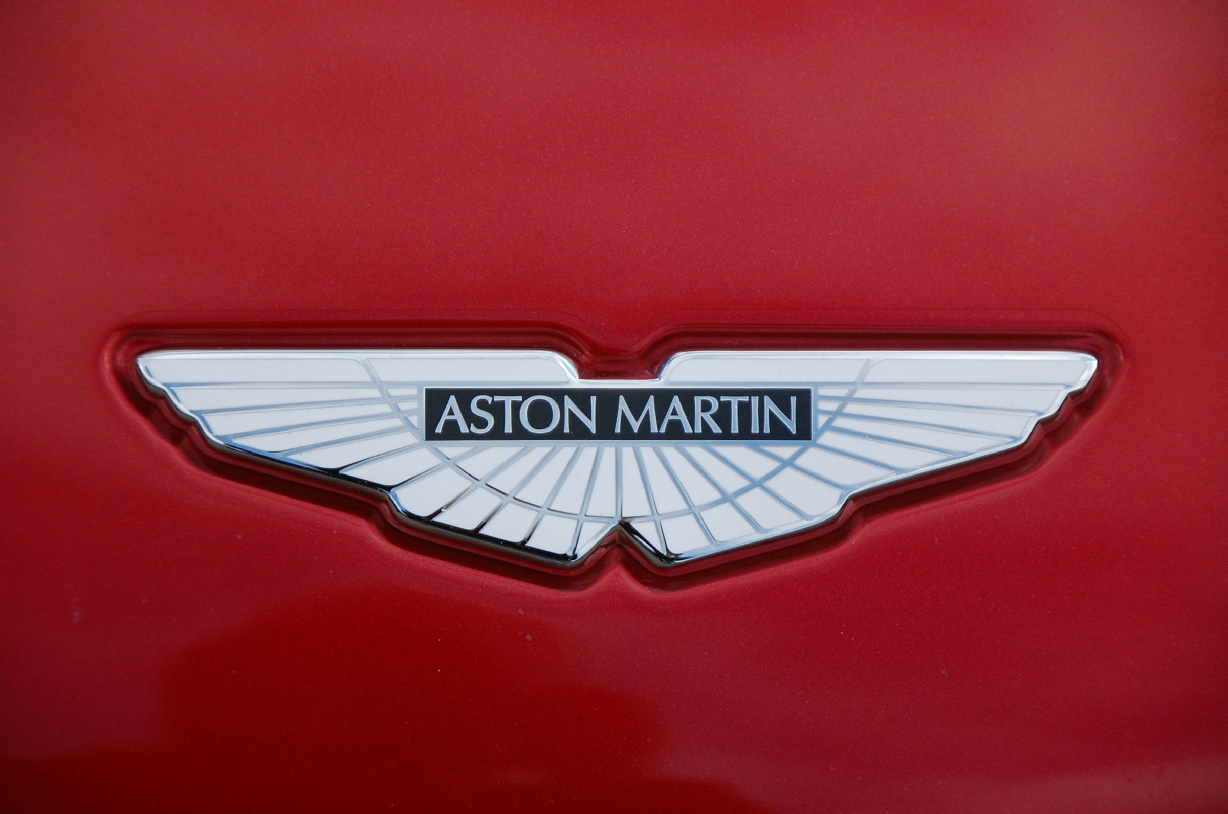 Close-up photo of the silver Aston Martin wings badge on the red hood of a car.