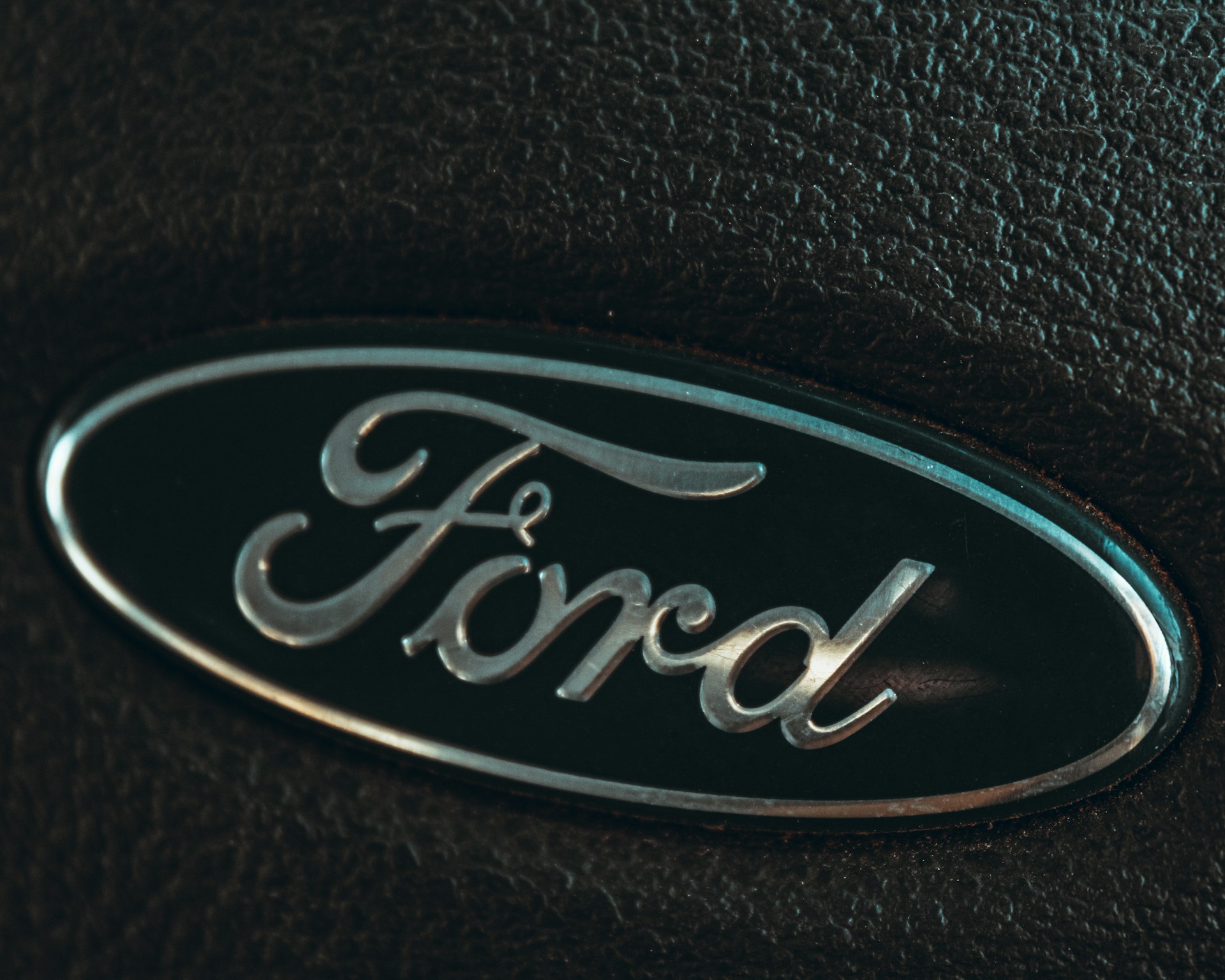 Close-up of a blue Ford logo on a black steering wheel.