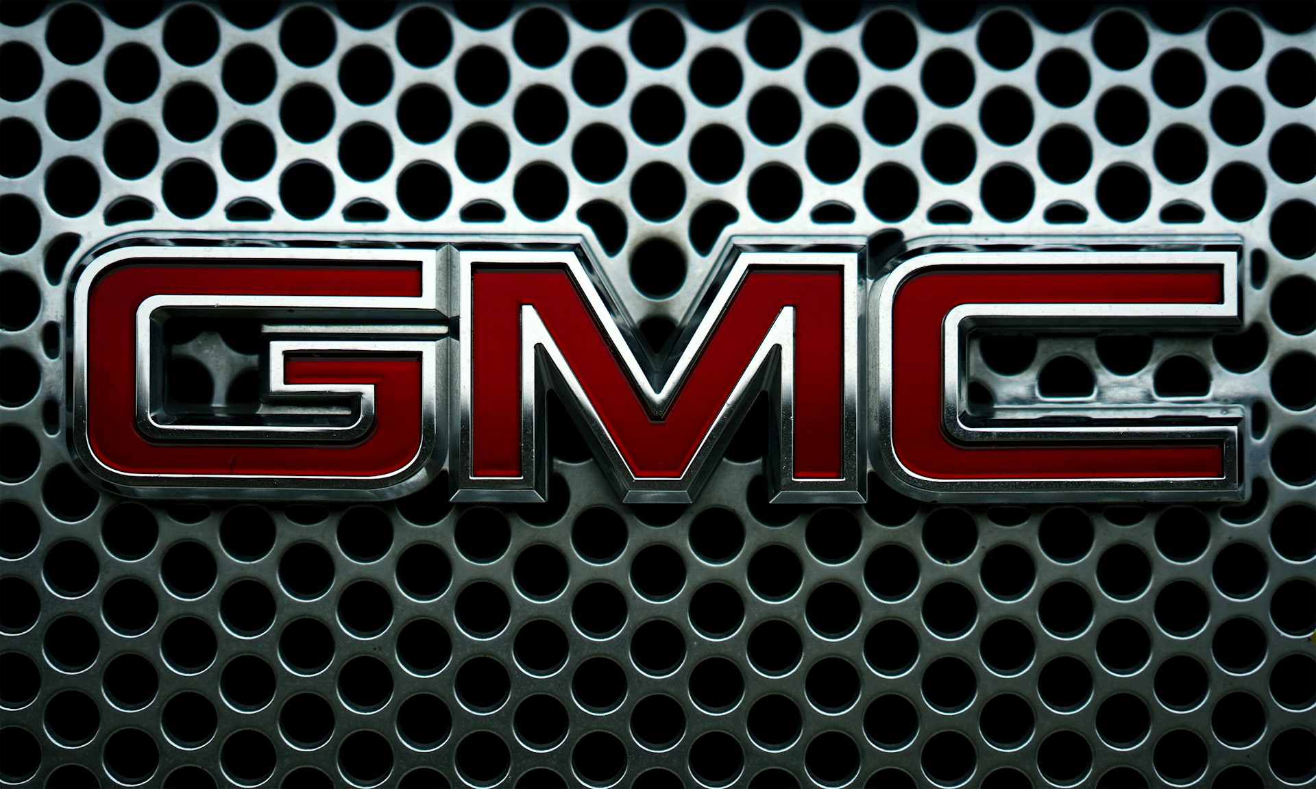 A close-up of the GMC logo on a grille with holes.