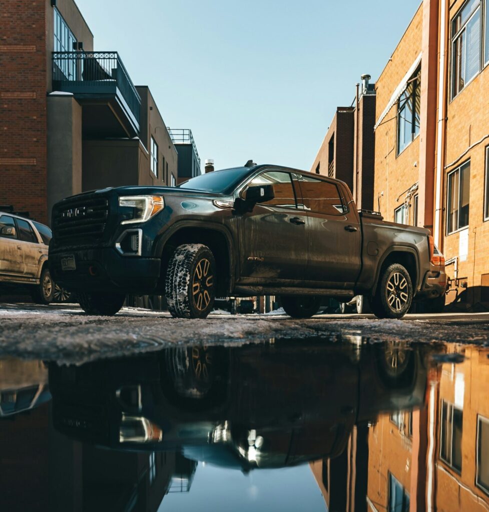 A black 2019 GMC Sierra 1500 AT4 pickup truck parked in a puddle in a city alleyway.