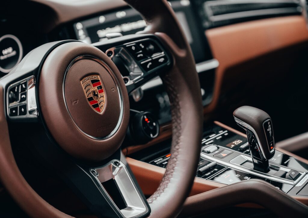 A close-up of a brown leather steering wheel with a Porsche logo on it.
