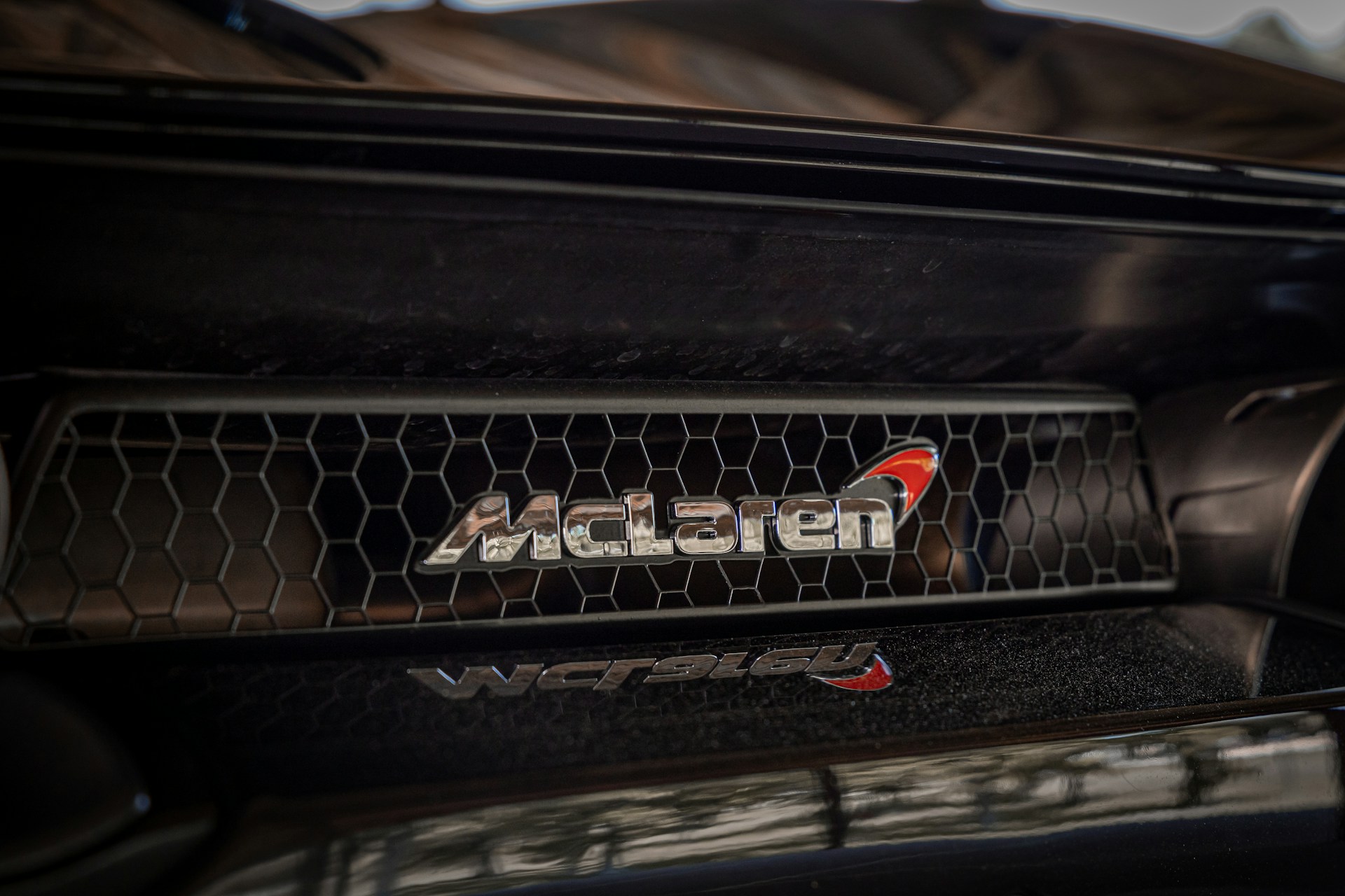 Close-up of a silver McLaren logo with a chrome border, featuring the iconic kiwi and speedmark.