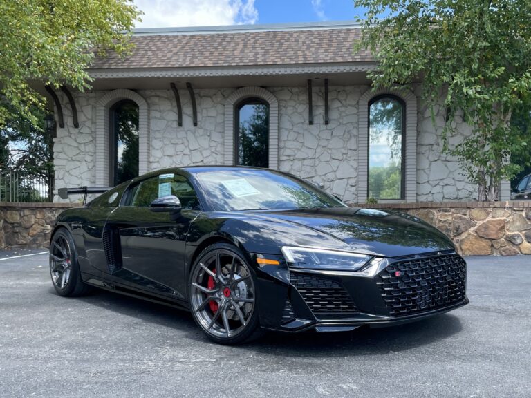 Black 2023 Audi R8 V10 Plus (Performance) with a sleek design, parked in front of a stone building with a lush green backdrop.
