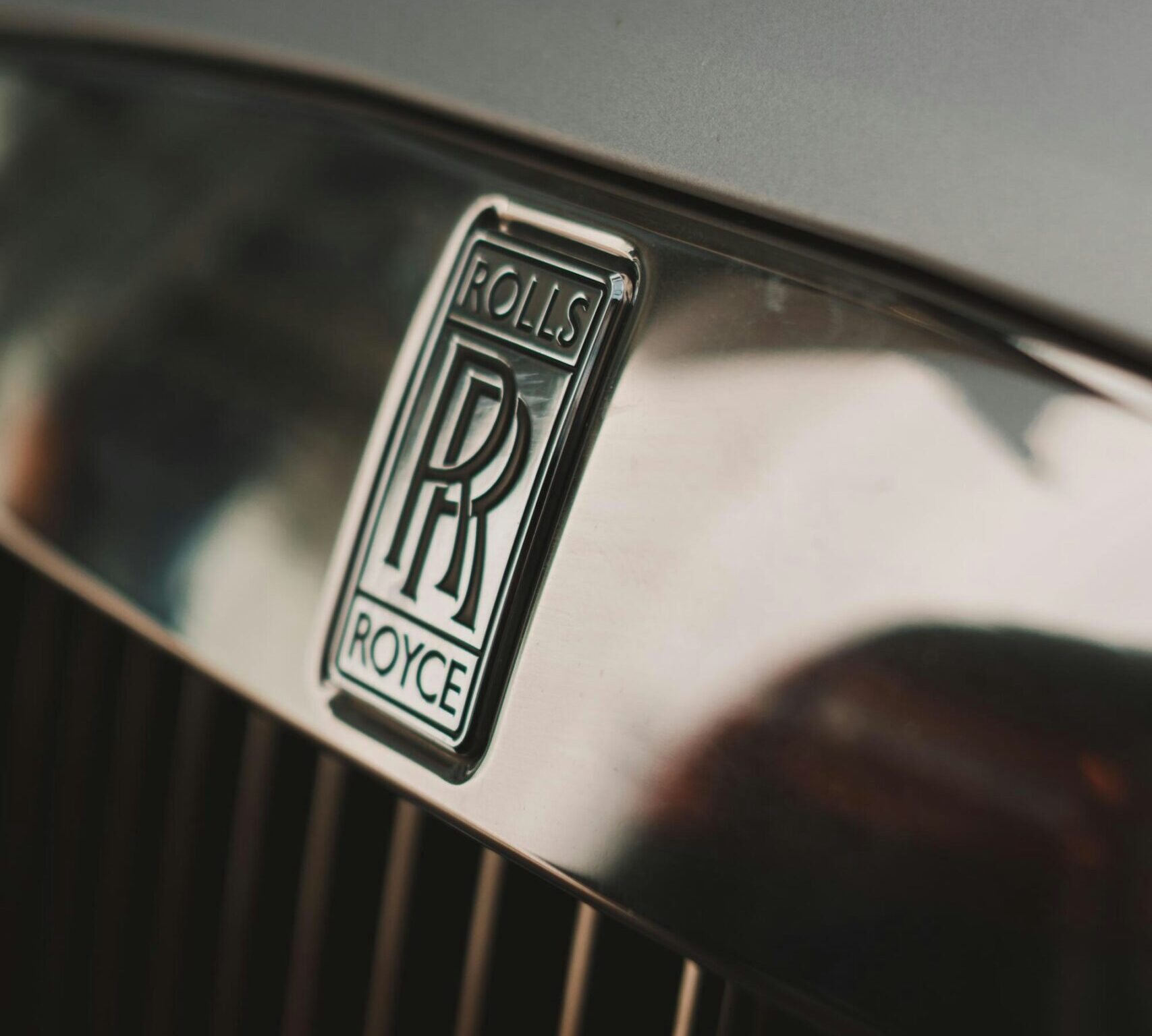 A close-up photo of a Rolls-Royce logo on the front grille of a car.