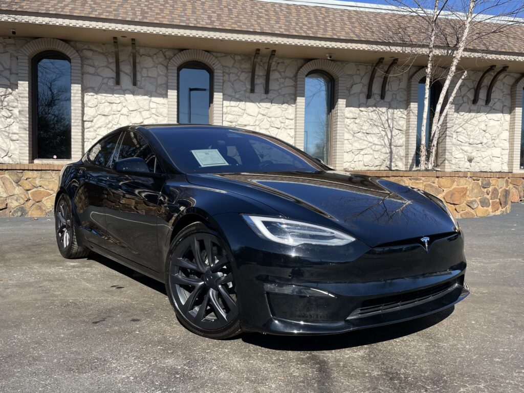 A black Tesla Model S parked in front of a stone building with a large glass window display