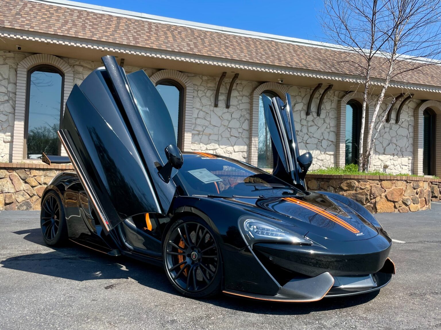 A black McLaren 570S sports car with its doors open is on display in the showroom of AutoPro Nashville, a used car dealership.