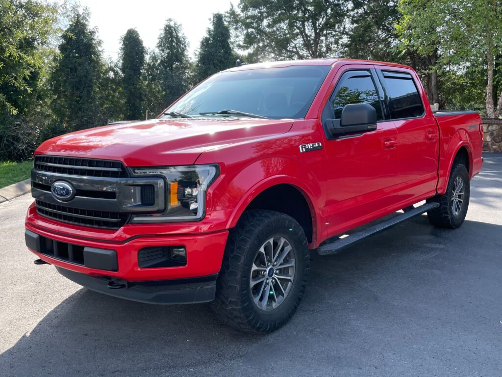 A red 2019 Ford F-150 XLT parked in AutoPro Nashville parking lot, with off-road tires and a lifted suspension.