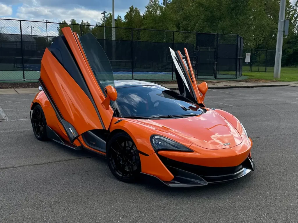 McLaren 600LT in McLaren Orange with butterfly doors open in parking lot.