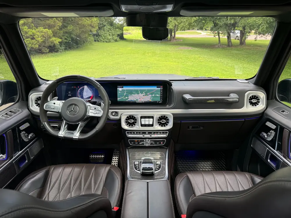 Interior of Mercedes-Benz G 63 AMG with carbon fiber trim, AMG steering wheel, and widescreen cockpit display.