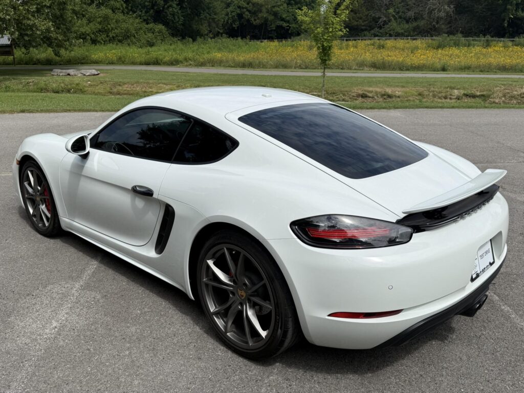 Rear view of a white 2019 Porsche 718 Cayman S with retractable spoiler, red brake calipers, and dark alloy wheels.