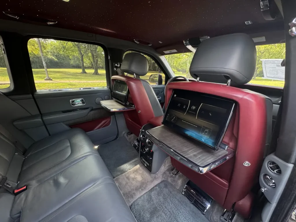 Rear luxury seats and dual infotainment screens inside a 2020 Rolls-Royce Cullinan with starry headliner.