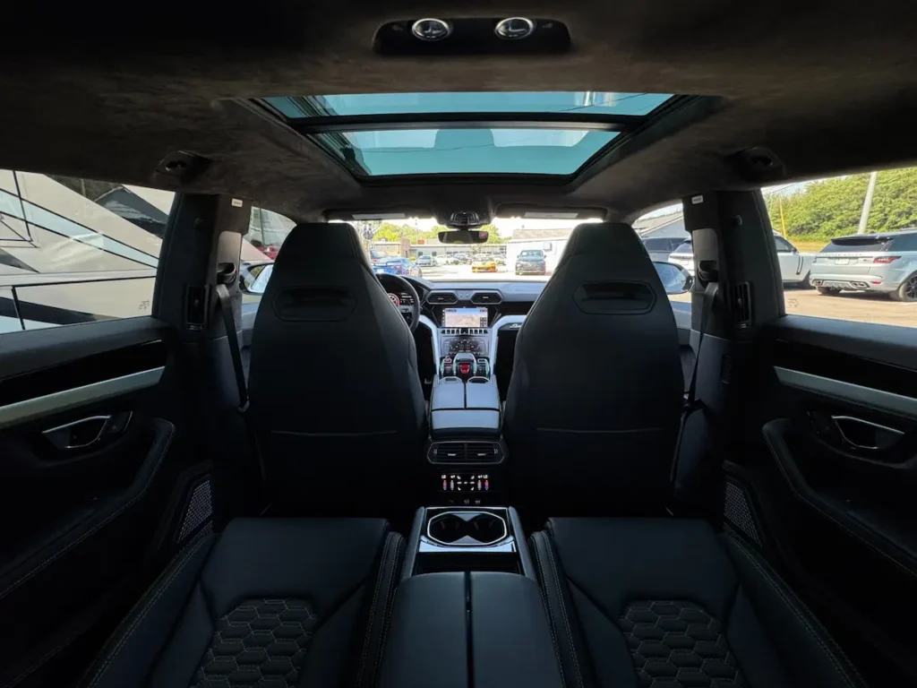Rear interior of Lamborghini Urus showcasing panoramic roof and black leather seating.