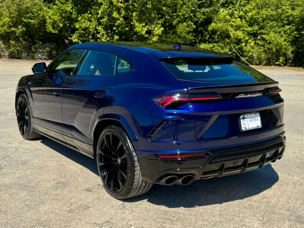 Rear angle of a 2021 Lamborghini Urus in metallic blue showing black alloy wheels and quad exhaust.