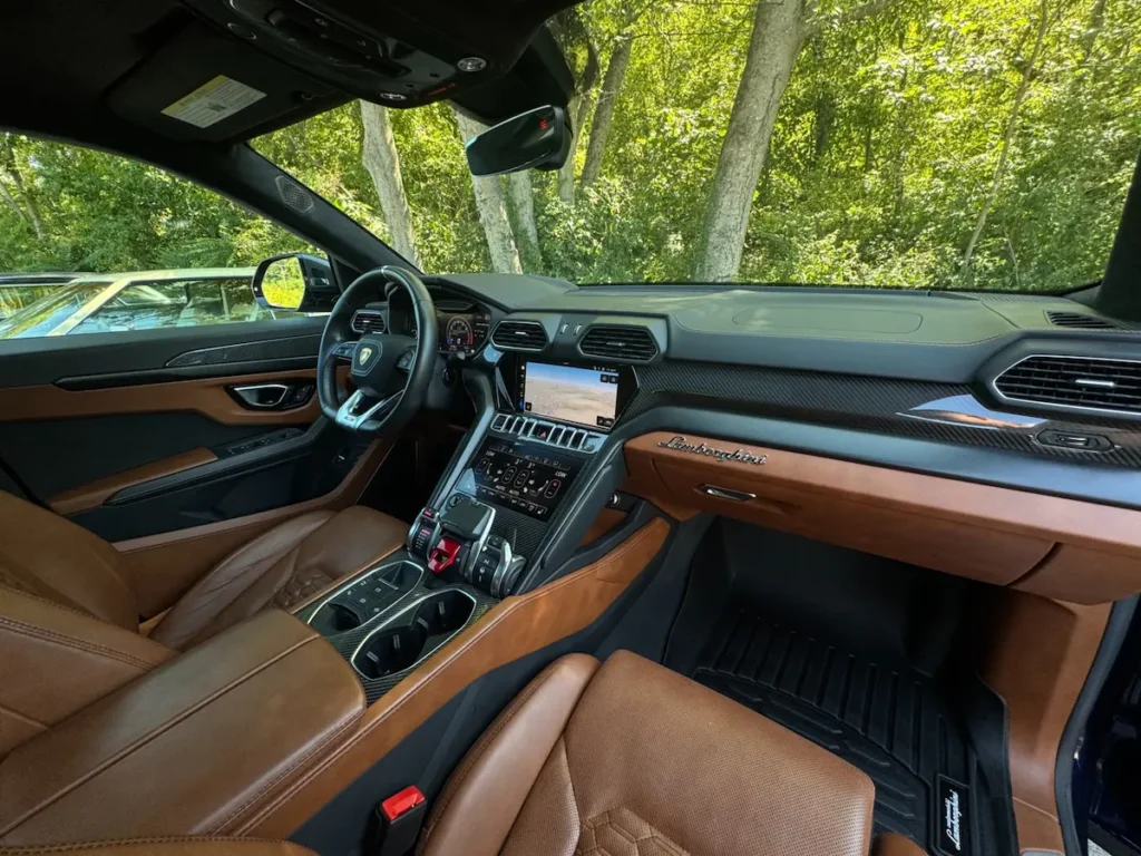 Lamborghini Urus front cabin view with dual touchscreens and carbon fiber trim.