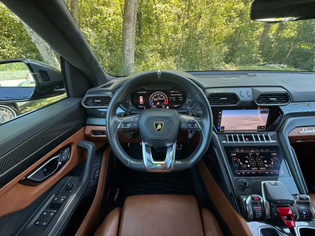 Interior view of 2021 Lamborghini Urus showing steering wheel, carbon-fiber dashboard, and digital cockpit display.