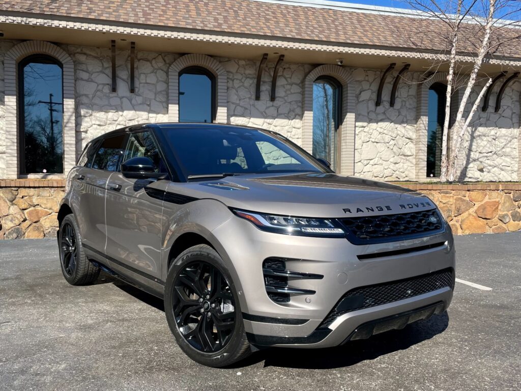 A silver Range Rover Evoque parked in front of the stone showroom of AutoPro Nashville, a used car dealership.