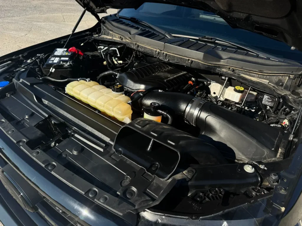 Engine bay of a Ford F-150 showing supercharged V8 setup and upgraded intake system.