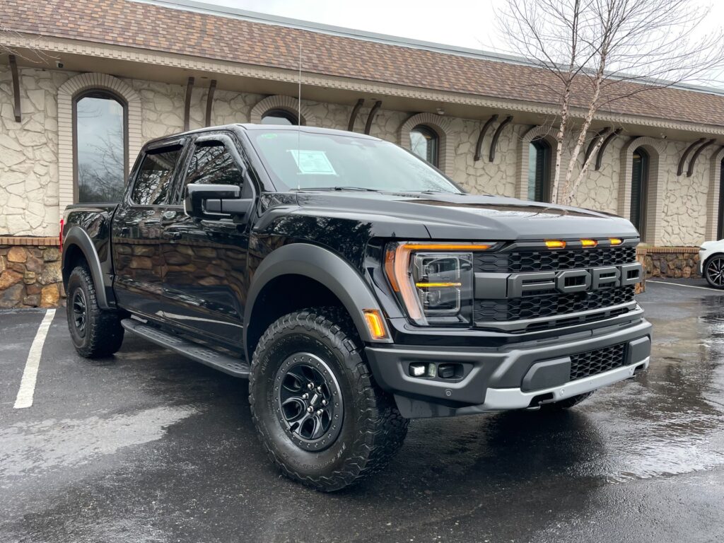Black Ford F-150 Raptor truck parked in front of a brick building with a large glass window at AutoPro Nashville Ford dealership.
