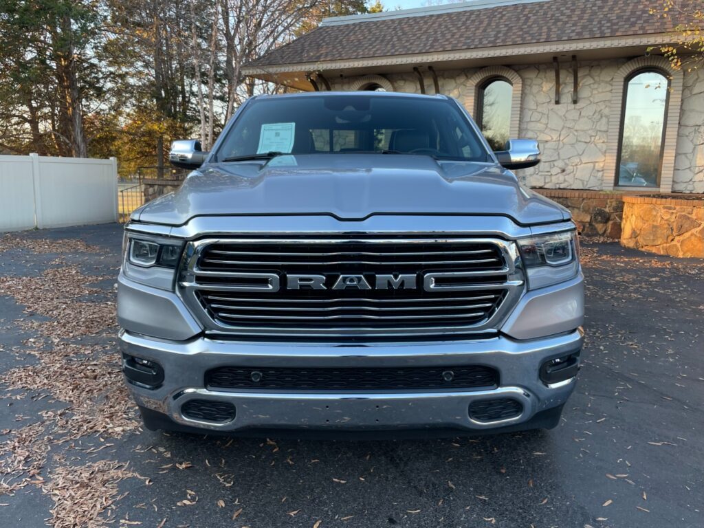 A silver Ram 1500 pickup truck with chrome accents parked in a dealership parking lot.