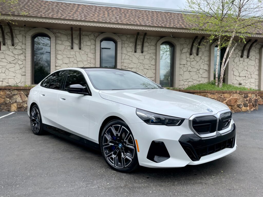 White BMW i5 electric car parked in front of a gray stone building with a black awning and large windows.