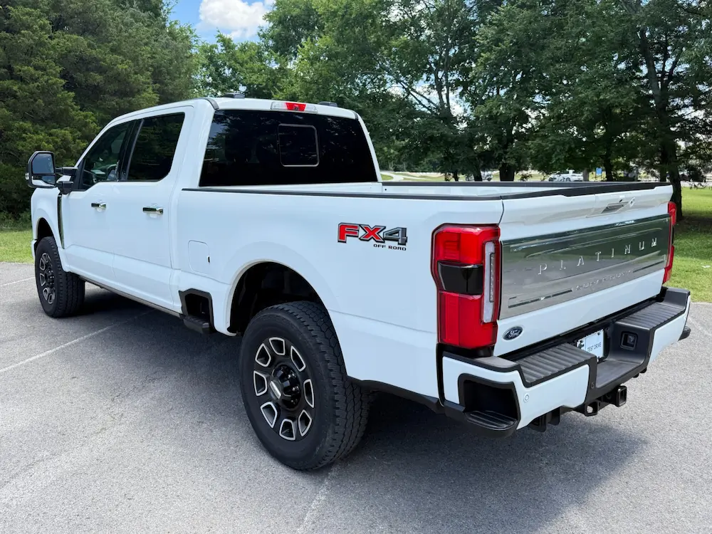 Rear three-quarter view of a 2024 Ford F-350 Super Duty Platinum FX4 Off-Road pickup in white with chrome tailgate accents.