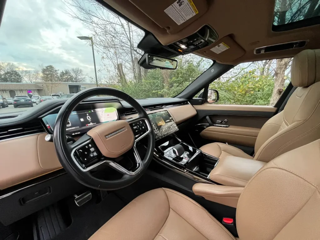 Front interior of a Range Rover with tan leather, digital cluster, and panoramic roof.