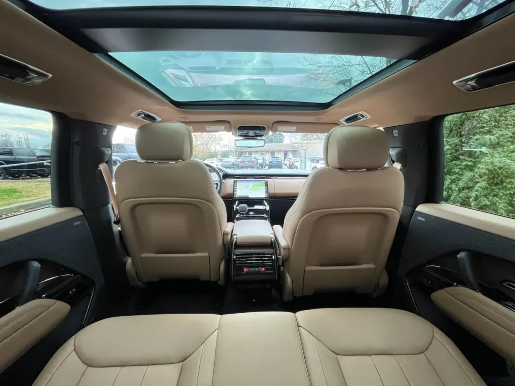 Rear cabin of a Range Rover with tan leather seats and panoramic roof.