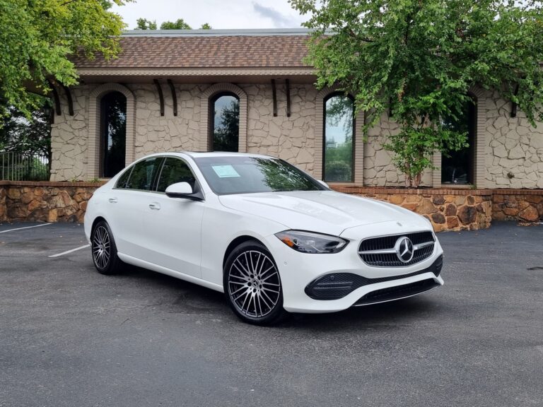A white Mercedes-Benz C-Class sedan parked in front of a brick building with trees in the background. The car is for sale at Autopro Nashville, a used car dealership.