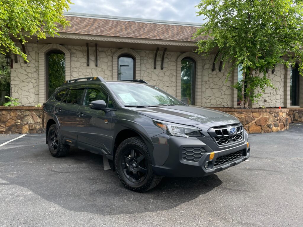 A gray 2024 Subaru Outback Wilderness SUV parked in front of the AutoPro Nashville dealership.