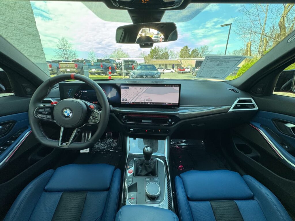 Luxurious interior of the 2025 BMW M3 featuring carbon fiber trim, a high-tech digital display, and sporty blue leather seats.