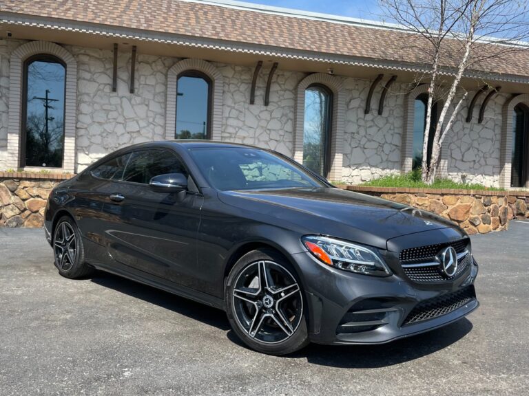 A black used 2022 Mercedes-Benz C-Class coupe parked in front of a stone building. The car is for sale at Autopro Nashville, a used car dealership.