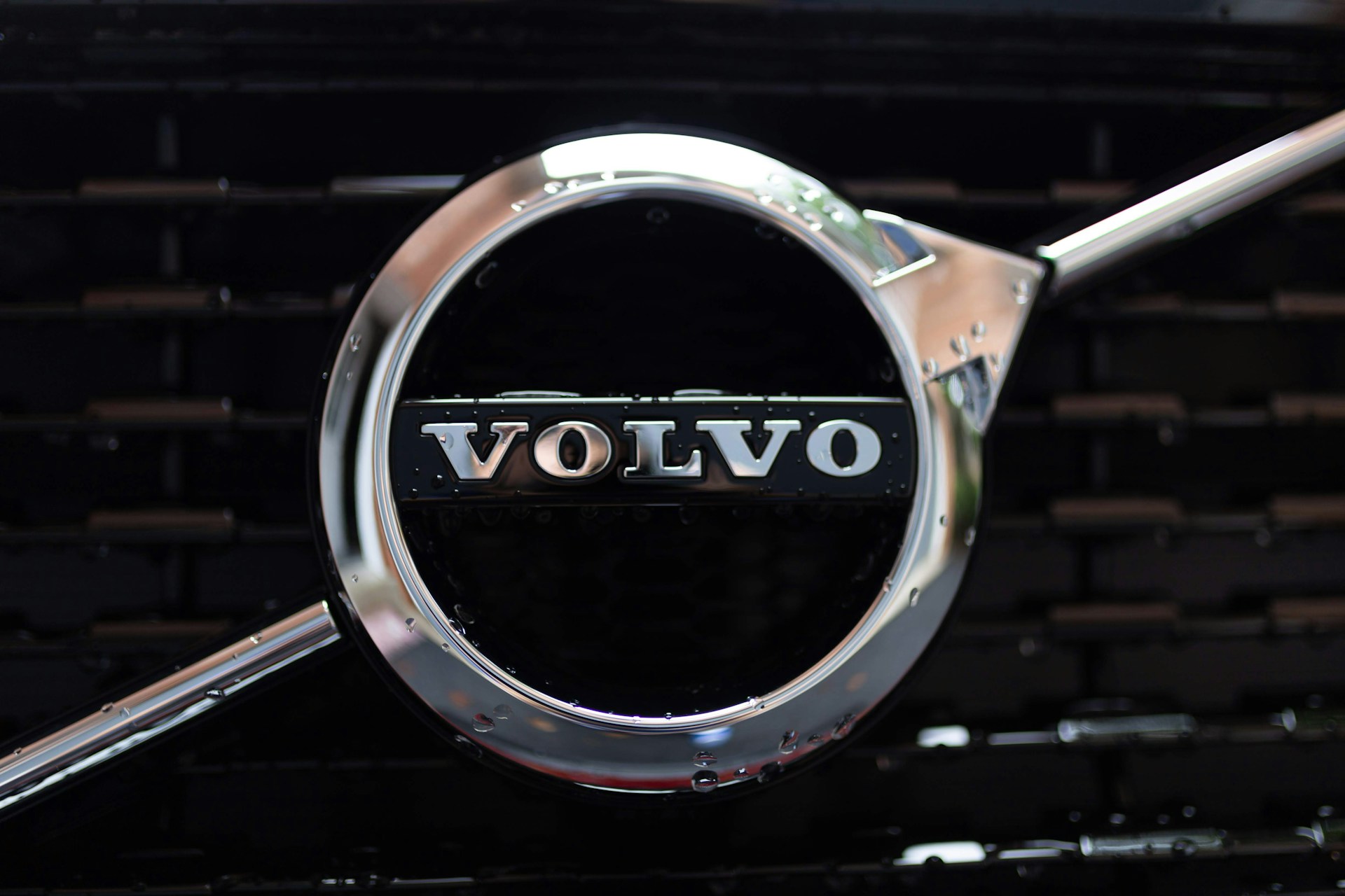lose-up photo of a silver Volvo logo on the chrome grille of a black car.